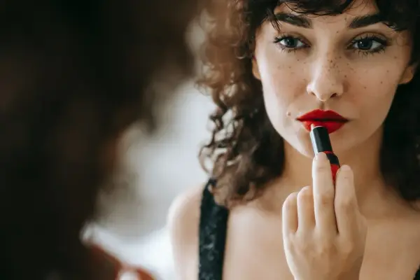 Donna con capelli ricci applica un trucco con rossetto rosso vibrante, creando un look audace e seducente.